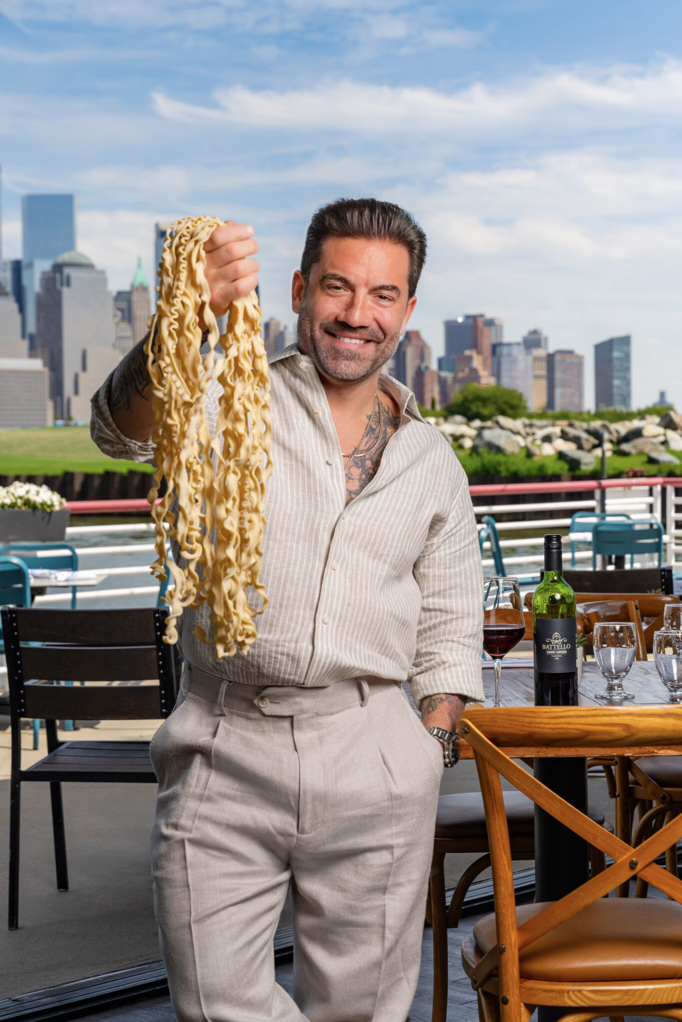 Chef Ryan DePersio holds up a fistful of pasta outside his restaurant Battello in Jersey City, NJ, with the Manhattan skyline behind him
