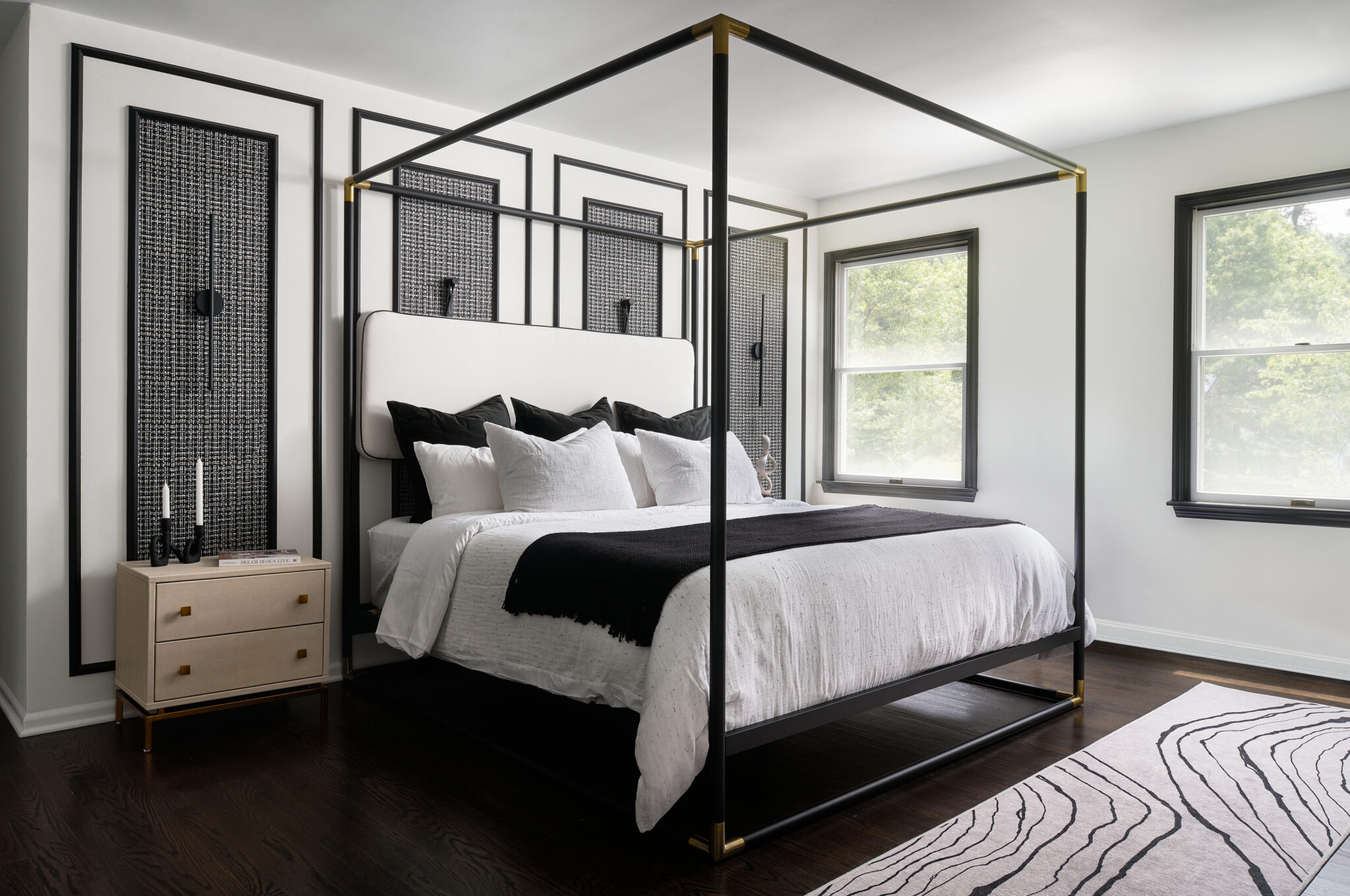 Inside a colonial home in Randolph, NJ, the primary bedroom—modern and high-contrast in black and white—showcases inset panels lined with Phillip Jeffries woven wallpaper and a CB2 metal bed frame customized with a cushioned headboard.