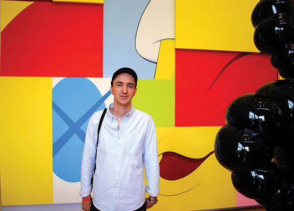 Brian Donnelly (alias KAWS) stands before his 2010 mural, “The Wall.”