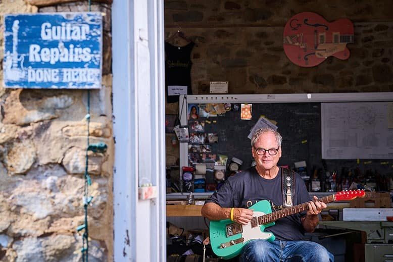 Craftsman Curt Wilson sits with a guitar at the entrance of his Old School Guitar–Repair, Restoration and Lutherie in Hopewell