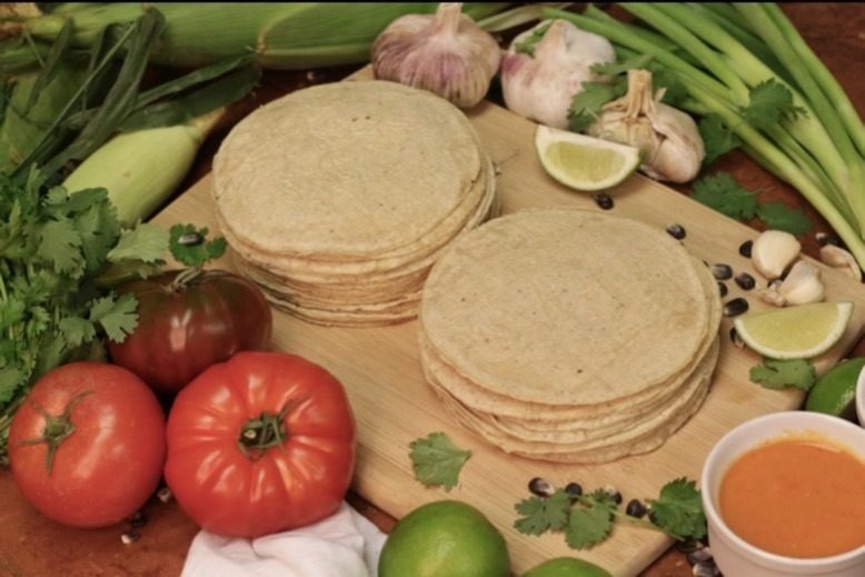Two stacks of tortillas made at Tortilleria Nixtamal in Woodland Park, surrounded by vegetables and herbs
