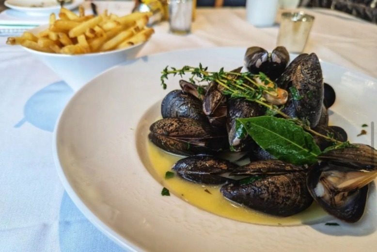 A platter of mussels in front of a bowl of fries