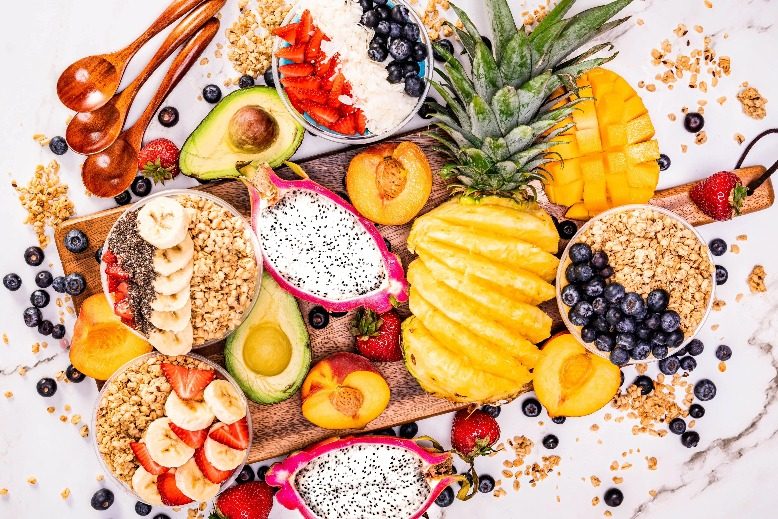 A table filled with dragon fruit, peaches, pineapple, blueberries, strawberries and avocado