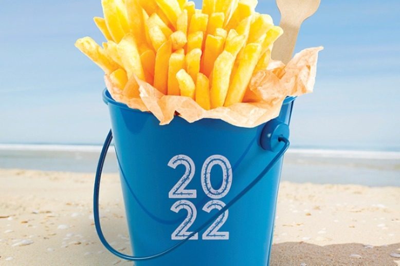Fries in a bucket sitting on a beach.