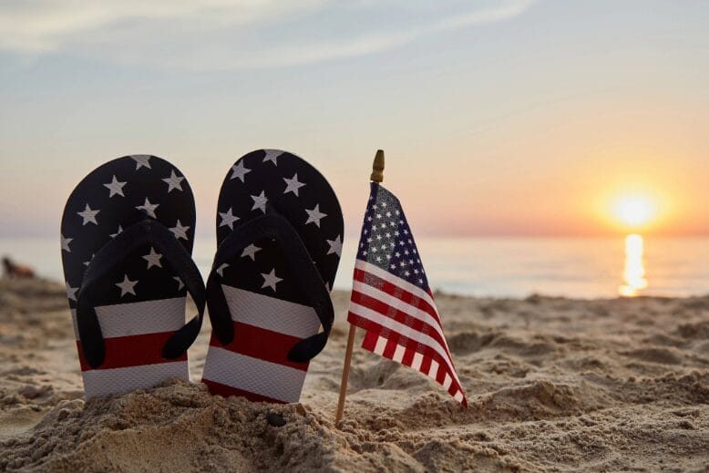 American flag and American flag flip-flops in sand at beach at sunset