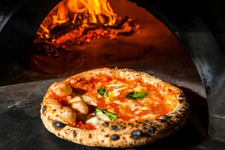 Pizza coming out of wood-burning oven