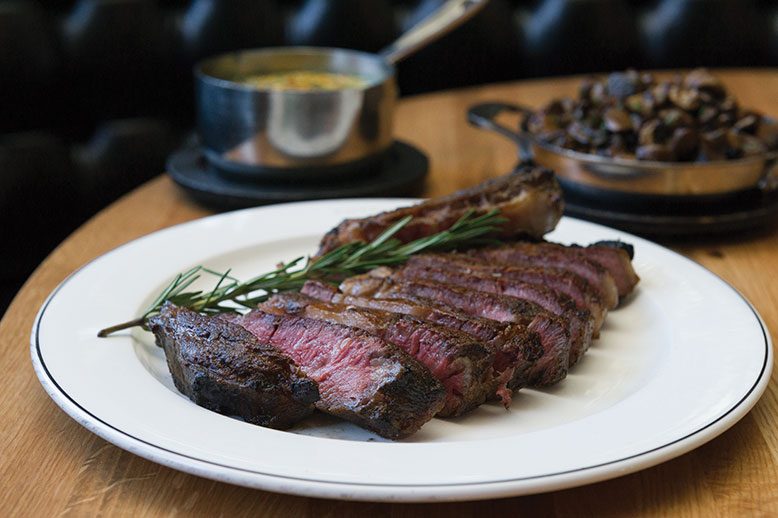 The expertly charred garlic-and-herb-rubbed bone-in sirloin, sliced, with a pan of wild mushroms on the side.