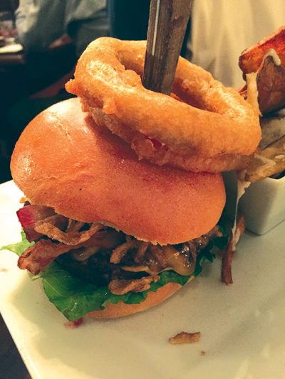 The signature Claremont Burger, with bacon, frizzled onions and cheddar on a brioche bun topped with two crispy onion rings made with red onions.