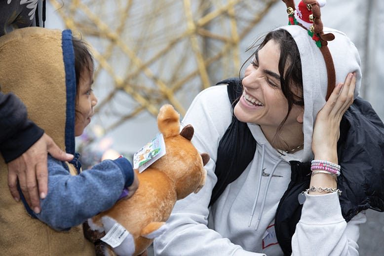 Woman with reindeer ears talks to young child holding stuffed animal