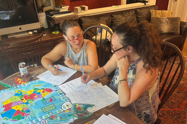 Two Montclair moms working at a table on their board game, "Dad in Chad"